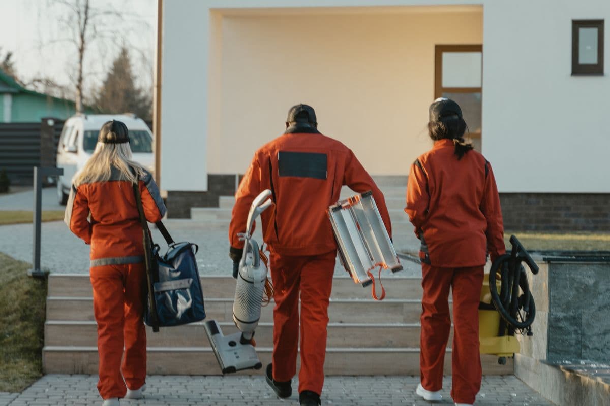 Equipo de limpieza uniformado caminando hacia una casa con su equipo