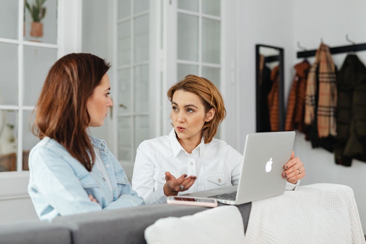 Dos mujeres sentadas en casa, una explicando algo con las manos mientras la otra escucha