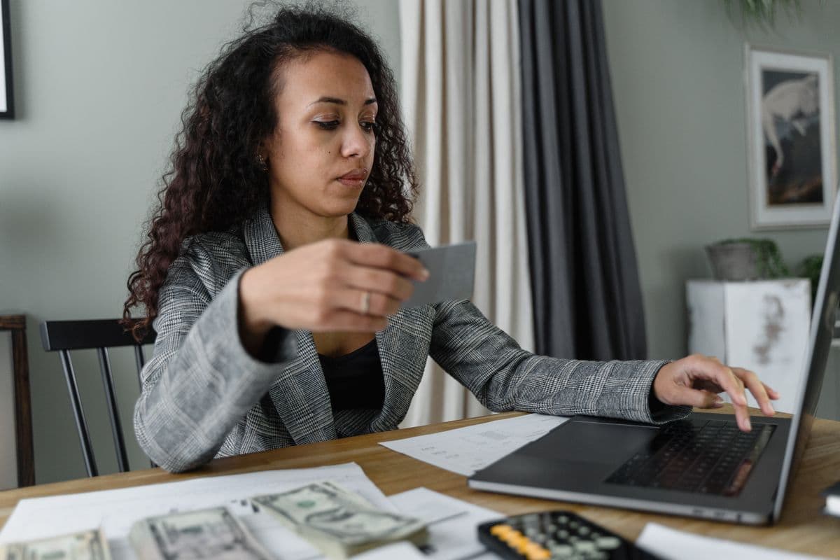 Mujer en la mesa sosteniendo una tarjeta, con efectivo, papeles y laptop