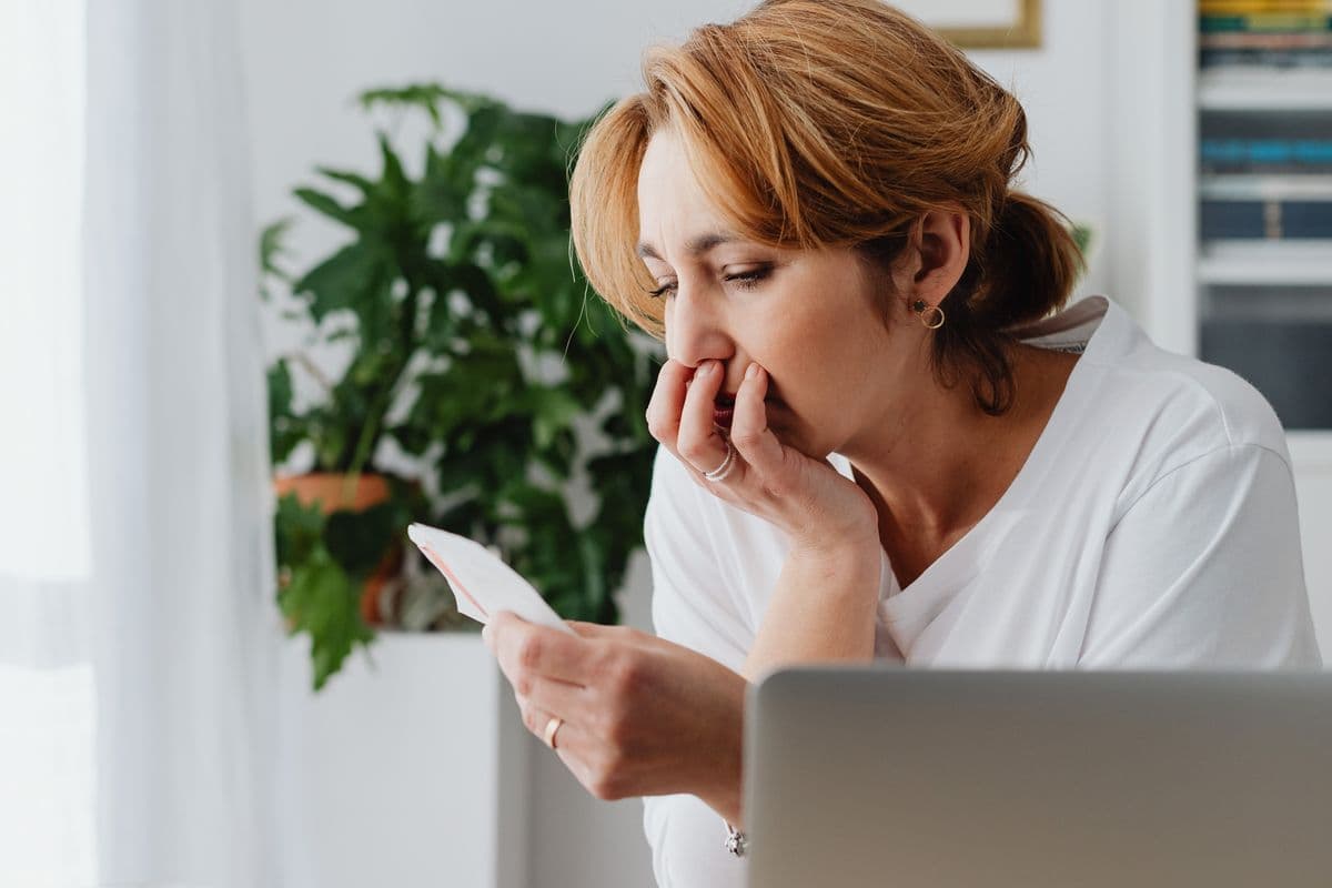 Mujer mirando con preocupación un recibo junto a la laptop
