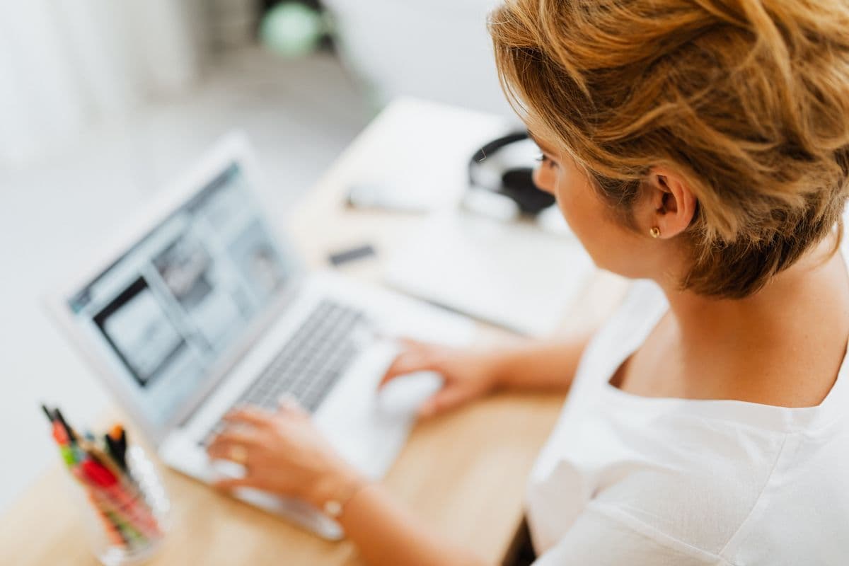 Mujer en un escritorio en casa, con la pantalla de la laptop mostrando el diseno de un sitio web